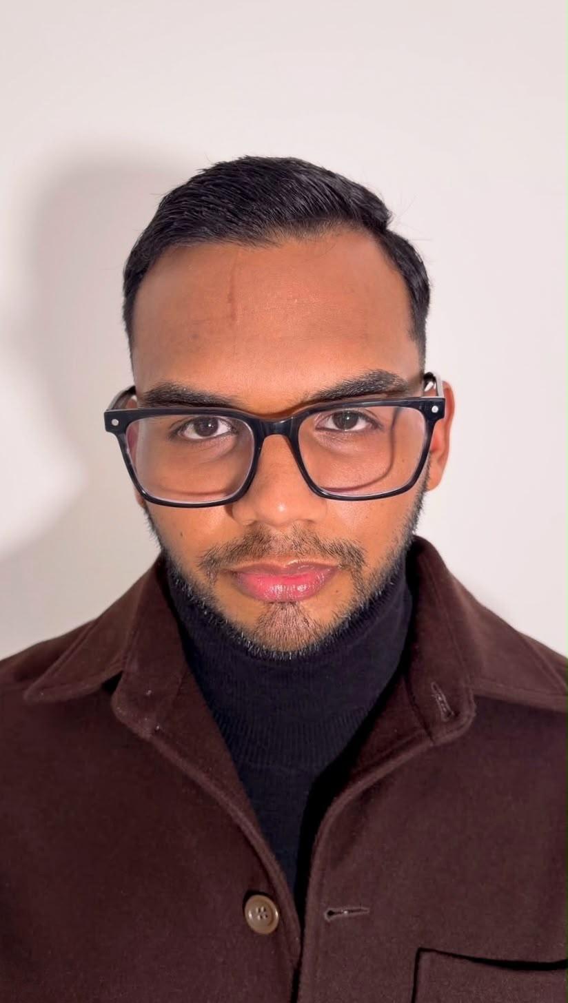 Portrait of Yosef Blandin wearing glasses, a black turtleneck and a brown jacket